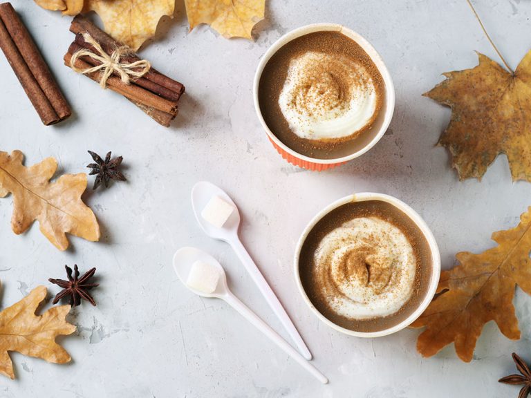 Two paper cups with tasty pumpkin latte and spice on gray table with autumn leaves. Top view. Closeup