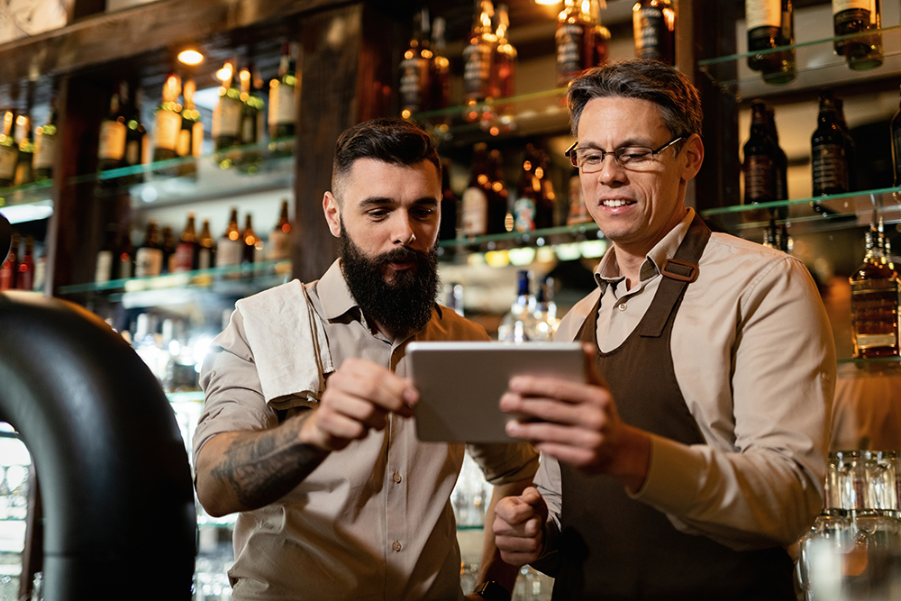 Two bartenders using digital tablet while working in a bar