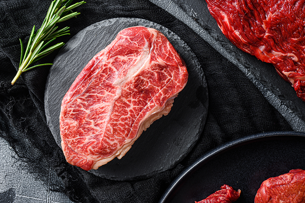 Raw top blade cut black angus organic  steak on a black plate an