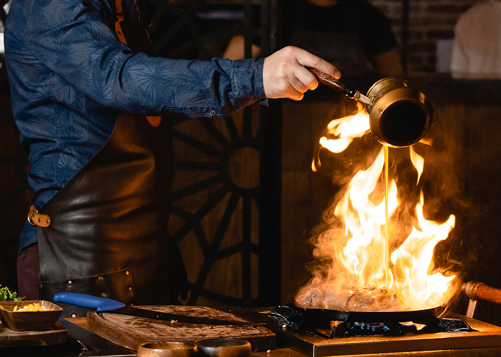 waiter pours oil into burning steak on the frying pan