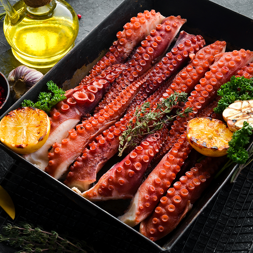 Boiled octopus tentacles with spices and herbs in a metal baking dish. Top view. Flat lay.