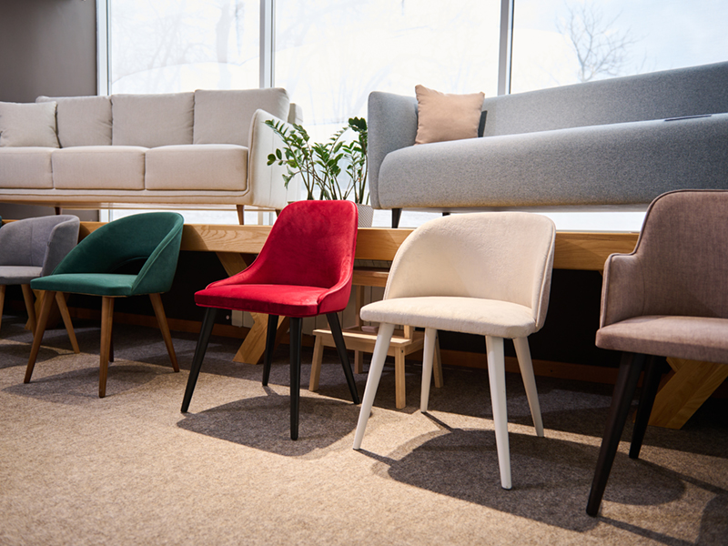Beautiful modern retro style colorful chairs, on dispay for sale in the furniture store showroom with settees, couches and sofas in light pastel colors on the background